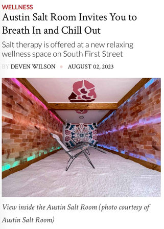Salt-therapy room in Austin with pink Himalayan salt brick walls, colorful LED mood lighting, two reclining lounge chairs on a white salt floor and a decorative mural.