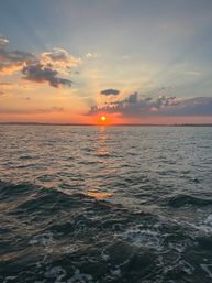 Serene coastal sunset over the ocean with the golden sun dipping below the horizon, colorful clouds and sunbeams reflected on rippling waves.