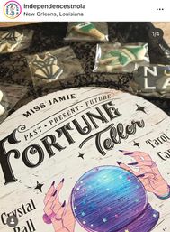 Close-up of a vintage-style 'Fortune Teller' sign with illustrated hands and a purple-blue crystal ball on black lace, surrounded by individually wrapped themed cookies, New Orleans.
