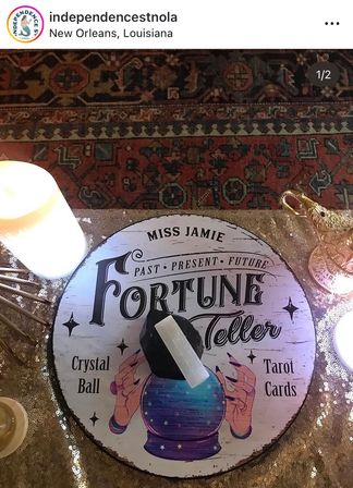 Fortune-teller display in New Orleans — round sign reading “Fortune Teller” with illustrated crystal ball, selenite wand on a stand, lit candles and ornate brass lamp on a sequin-covered table over a patterned rug