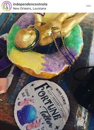 Mardi Gras king cake topped with a gold baby figurine and purple, green and gold beads next to a vintage-style fortune teller sign with a crystal ball — New Orleans table display