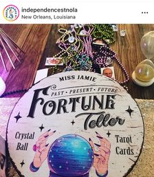 Round vintage fortune-teller sign with illustrated crystal ball and the words Fortune Teller on a wooden table, surrounded by colorful Mardi Gras beads, tarot cards, crystals and an hourglass in New Orleans, Louisiana.
