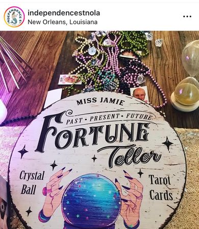 Round vintage fortune-teller sign with illustrated crystal ball and the words Fortune Teller on a wooden table, surrounded by colorful Mardi Gras beads, tarot cards, crystals and an hourglass in New Orleans, Louisiana.