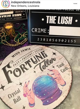 Round vintage fortune-teller sign with a colorful crystal ball illustration, tarot cards, candle and green-and-gold Mardi Gras beads arranged on a table in New Orleans.