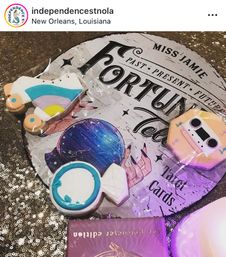 Bright decorated sugar cookies — roller skate, cassette, wrapped candy and round candy — arranged on a fortune-telling tarot sign and glittery sequin tablecloth in New Orleans, Louisiana.