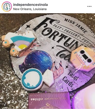 Bright decorated sugar cookies — roller skate, cassette, wrapped candy and round candy — arranged on a fortune-telling tarot sign and glittery sequin tablecloth in New Orleans, Louisiana.