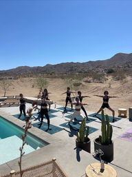 Outdoor poolside yoga — group of women in warrior poses on mats on a sunny desert patio with rocky hills and clear blue sky
