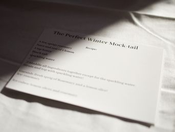 Cozy recipe card titled "The Perfect Winter Mock-tail" listing rosemary, lemon, honey and sparkling water on a white linen table with soft shadows.