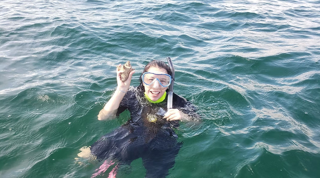 Smiling snorkeler in a wetsuit and mask floating in green ocean water, holding up a starfish beside a snorkel tube.