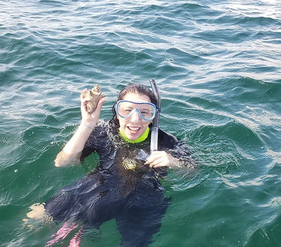 Smiling snorkeler in a wetsuit and mask floating in green ocean water, holding up a starfish beside a snorkel tube.