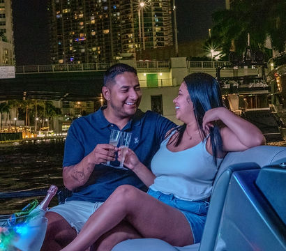 Smiling couple toasting with champagne on a yacht at night, city skyline and marina lights reflecting on the water