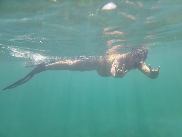 Snorkeler floating near the water’s surface in clear turquoise ocean, giving both hands a playful shaka (hang loose) sign