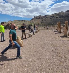 People participating in outdoor axe throwing on a rocky desert range with wooden target boards and rugged mountains under a partly cloudy sky