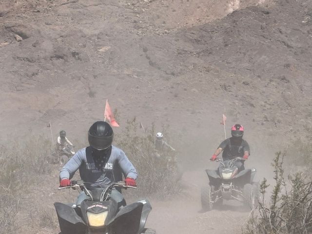 Off-road ATV riders in helmets with orange safety flags kicking up dust on a rocky desert trail below rugged canyon walls