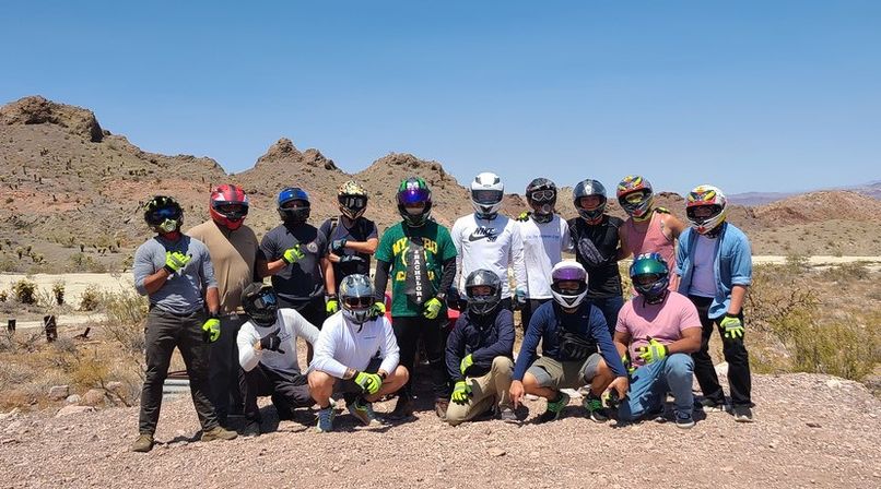 Group of off-road riders in helmets and neon gloves posing on a gravel trail with red rocky desert hills and a clear blue sky