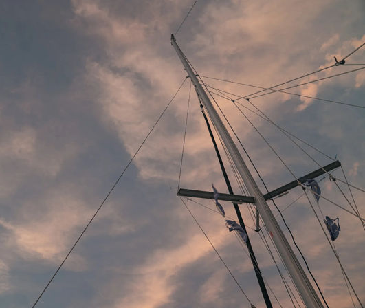 Sailboat mast and rigging silhouetted against a pink-tinged sunset sky with fluttering signal flags