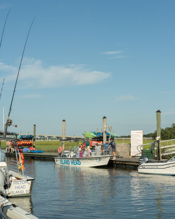 Tour boat loading passengers at a Hilton Head Island, SC marina with colorful kayaks stacked on the dock, calm reflective water and a clear blue sky