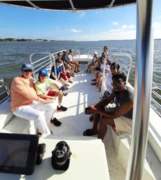Happy group seated on a white pontoon boat enjoying a sunny coastal bay cruise with calm water and blue sky