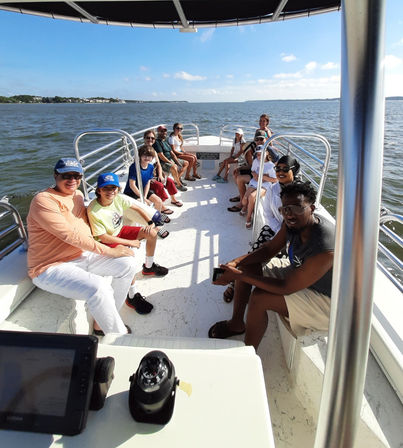 Happy group seated on a white pontoon boat enjoying a sunny coastal bay cruise with calm water and blue sky