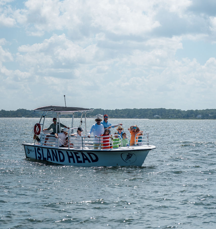 Sightseeing boat tour with adults and kids on a sunny summer day in a calm coastal bay, passengers wearing colorful life jackets and sun hats under a partly cloudy sky.