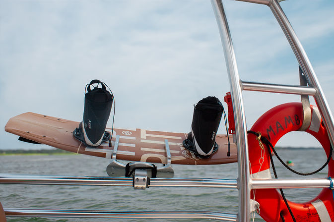 Wakeboard with boots mounted on a boat railing beside a red lifebuoy over a calm lake — summer water sports gear ready to ride