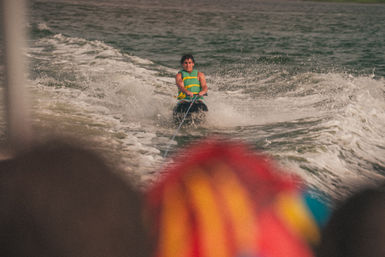 Rider in a green life jacket kneeboarding behind a boat on a choppy lake, spray and wake trailing