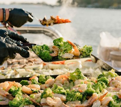 Steamy shrimp and broccoli sizzling on a flat-top grill at a waterfront outdoor cookout