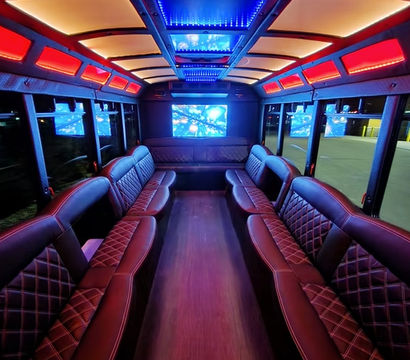 Luxury party bus interior with red and blue LED ceiling lights, quilted leather bench seating along both sides, hardwood aisle, and multiple flat-screen TVs.