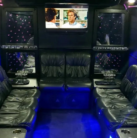 Luxury party bus interior with black leather wraparound seating, blue LED floor lighting, mirrored star-effect panels, cup holders and a wall-mounted TV