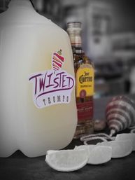 Plastic jug with a colorful "Twisted Trompo" sticker beside a tequila bottle, lime wedges and a striped spinning top on a bar counter