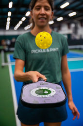 Action shot of a player on an indoor pickleball court holding a paddle as a bright yellow perforated pickleball hovers above it