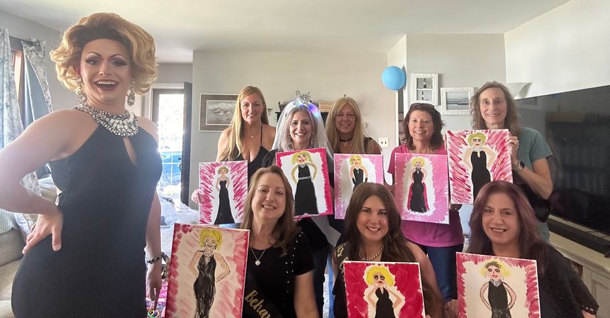 Indoor bachelorette paint party at home: bride-to-be wearing a veil and friends hold canvases of a blonde in a black dress while a glamorous drag performer poses at left