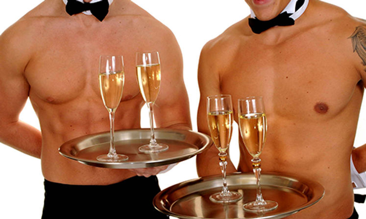 Close-up of two shirtless male servers wearing bow ties holding metal trays with four champagne flutes, playful party catering scene.