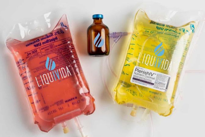 Pink and yellow IV therapy nutrient bags with tubing and a small amber vial on a white background — colorful vitamin hydration drip setup.