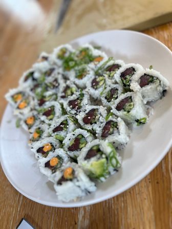 Assorted inside-out sushi rolls with tuna, avocado, scallions, sesame seeds and spicy mayo dots on a white plate over a wooden table