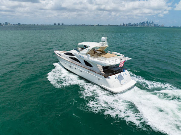 Luxury white motor yacht cruising turquoise waters near Miami skyline, leaving a foamy wake under a partly cloudy sky