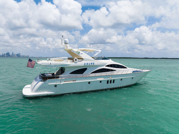 Luxury white motor yacht flying an American flag gliding on turquoise water with a distant city skyline and fluffy clouds