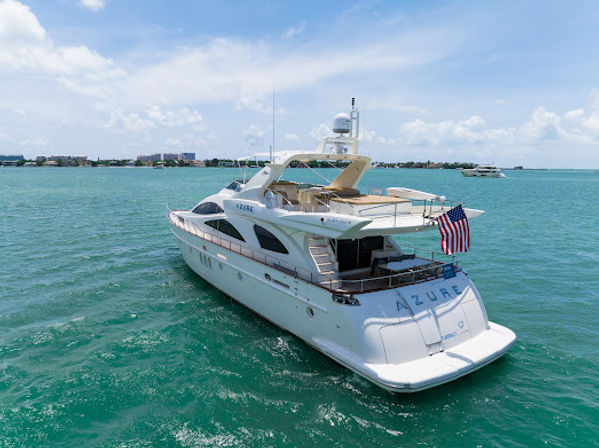 White luxury motor yacht with American flag cruising turquoise coastal waters under a sunny blue sky