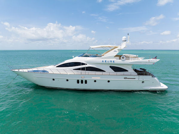White luxury motor yacht afloat on calm turquoise ocean under a sunny blue sky, side profile showing decks and flybridge