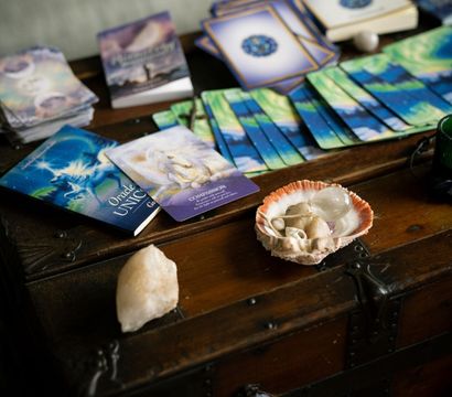 Colorful oracle cards, guidebooks and a seashell holding healing crystals arranged on a vintage wooden chest — cozy spiritual reading setup.