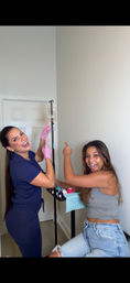 Cheerful clinician in scrubs with pink gloves and a smiling patient pointing at a hanging IV drip in a compact wellness clinic treatment room with a small medical tray.