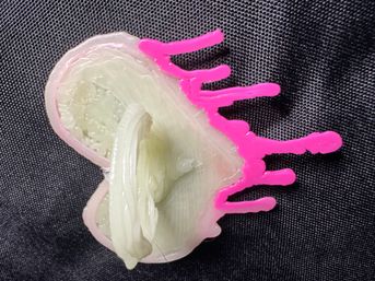 Heart-shaped resin geode trinket with pale green crystal center and neon pink drip accents on a black fabric background