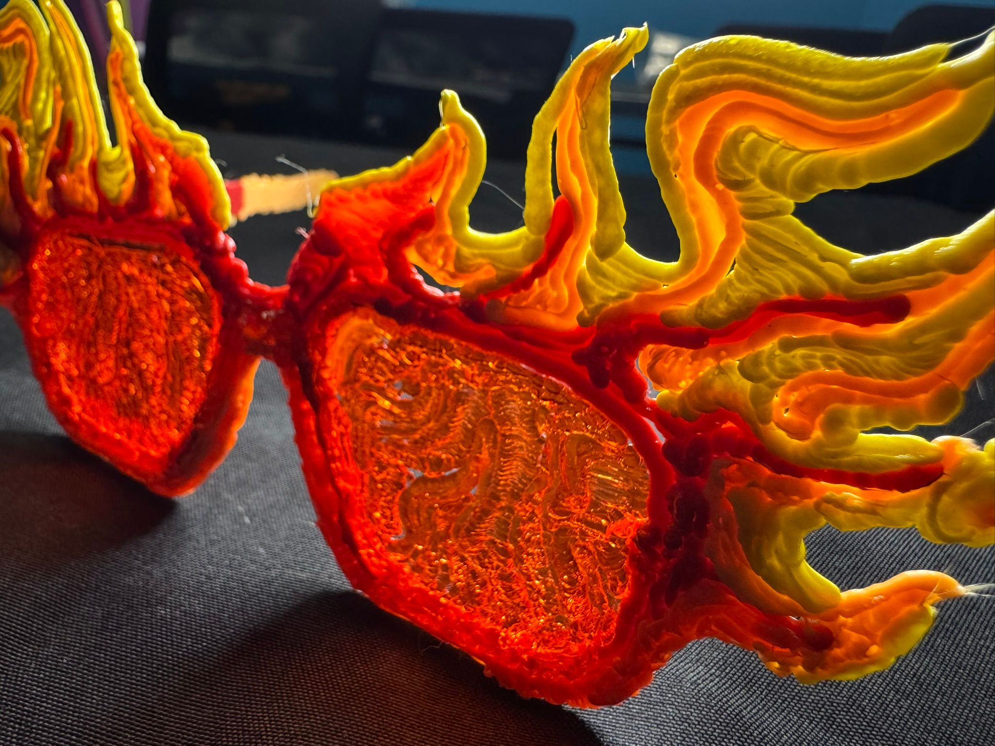 Close-up of fiery 3D-printed sunglasses with layered orange and yellow filament, sculptural accessory resting on black fabric