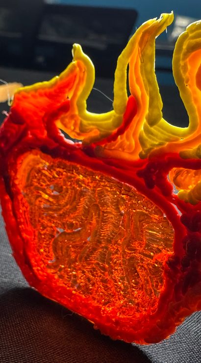 Close-up of fiery 3D-printed sunglasses with layered orange and yellow filament, sculptural accessory resting on black fabric