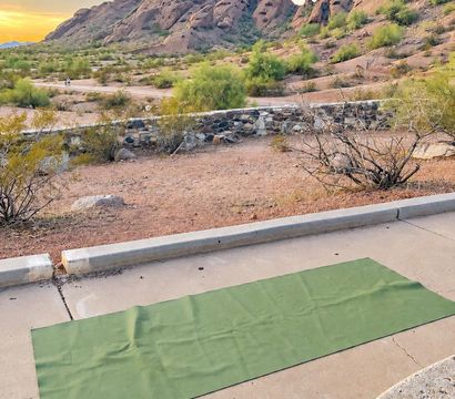 Green yoga mat laid on a concrete patio with desert scrub and dramatic sandstone rock formations at sunset in the Arizona desert.