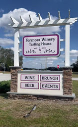 White pergola-style roadside sign for a winery tasting house with stone pillars; lower panels advertise WINE, BRUNCH, BEER, EVENTS against a bright blue sky.