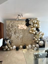 Indoor gold sequin backdrop with black-and-gold balloon arch and neon 'Til Death Do Us Party' sign, styled over marble floor and glass table for a glam celebration.