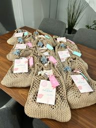 Beach-style woven tote favor bags with pastel pink and mint tags and flower charms neatly arranged on a wooden dining table in a modern home — perfect bridal shower or bachelorette party gifts.