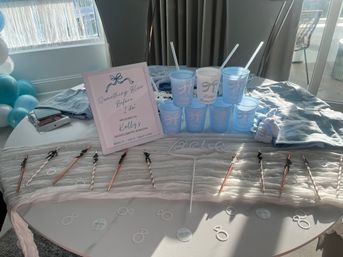 Sunlit bachelorette party table in light blue: framed "Something Blue Before I Do" sign, stacked blue plastic cups with straws, rose-gold and striped drink stirrers, ring-shaped confetti and coordinating balloons.
