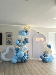 Indoor blue, navy and cream balloon garland and clusters framing a white arch backdrop with neon 'Let's Party' sign, modern coastal party decor